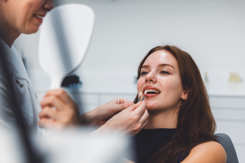 Dentist with a mirror and shade guide during a cosmetic dentistry consultation in New Lenox, IL